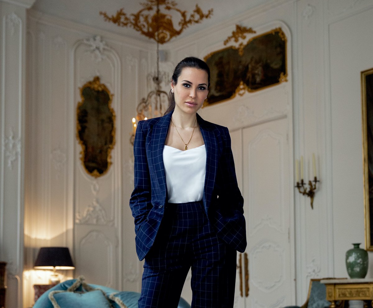 Bella French wearing a navy blue power suit stands and looks directly at the camera.