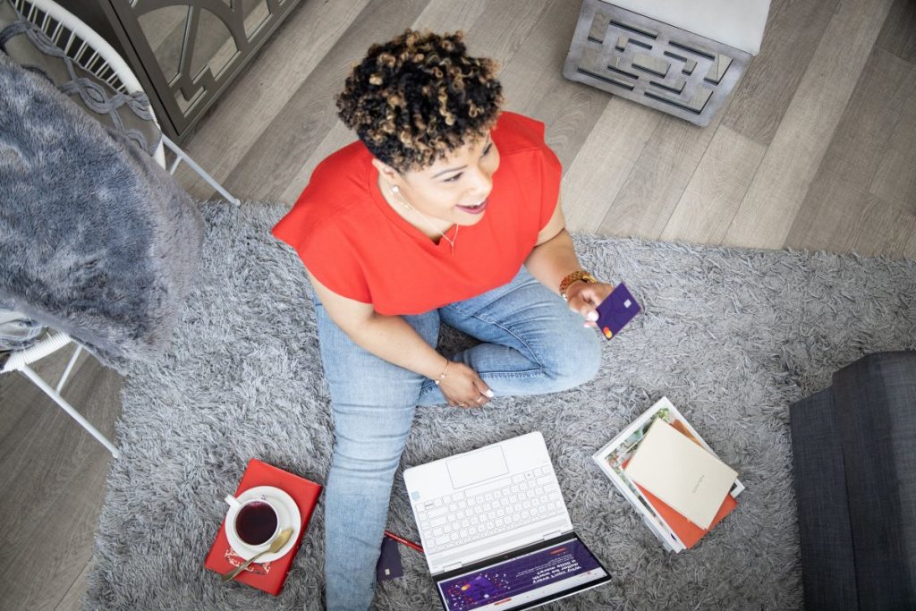 Vanessa Bowen, Creator of Mint Worthy in a red top and heans, sitting on the floor with her laptop, a coffee, some notepads and a credit card
