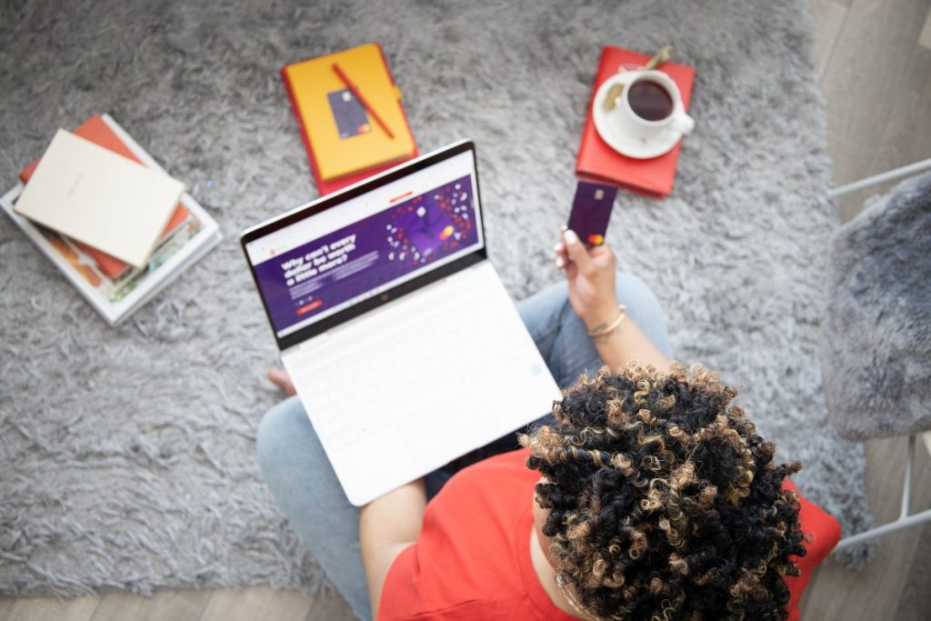Vanessa Bowen, Creator of Mint Worthy in a red top and heans, sitting on the floor with her laptop, a coffee, some notepads and a credit card