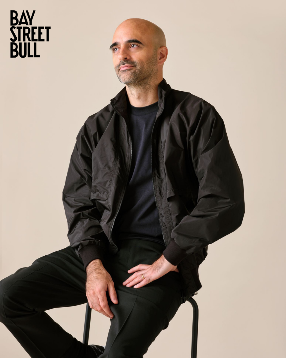 SSENSE CEO Rami Atallah looking off-camera wearing all black on a stool against neutral background