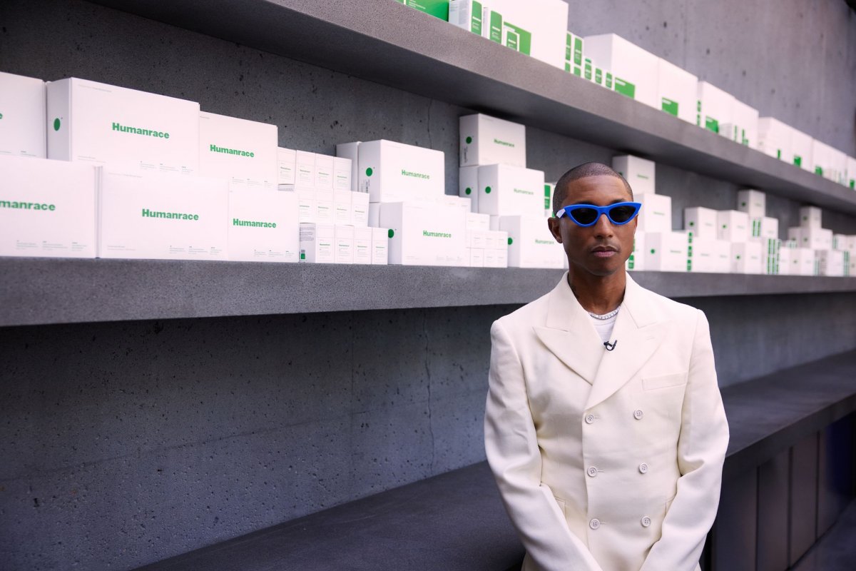 Pharrell wearing green sunglasses and white suit against wall of white packaging